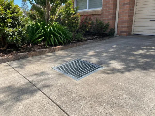 Flush stormwater grate set in a concrete driveway beside a brick house and garden in Baulkham Hills